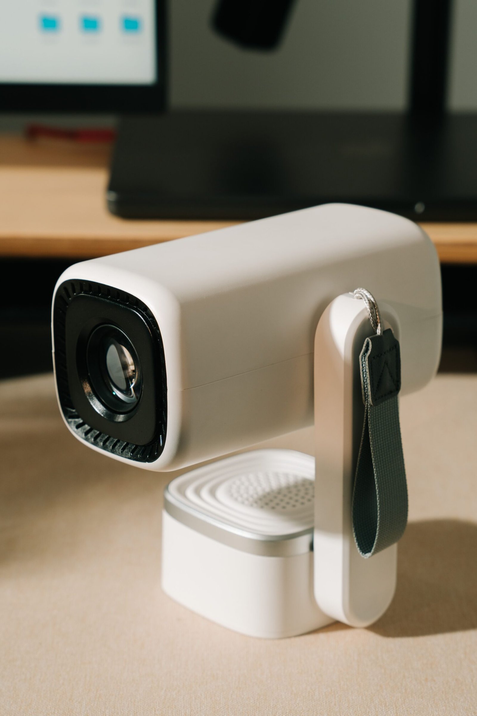 Home A sleek white portable projector with strap on a desk, perfect for home entertainment or business meetings.